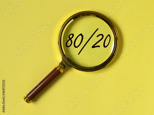 80 20 pareto principle concept, text through magnifying glass on yellow background.