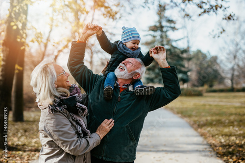 Happy senior couple walking and playing with their adorable grandson in public city park.