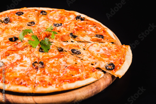 Pizza with olives and tomatoes on a wooden board on a black background