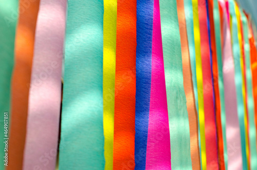 Background texture of bright and colorful rainbow crepe paper streamer backdrop with spotty sunlight.