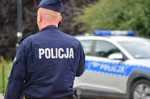 Policjant prewencji a w tle radiowóz policyjny.