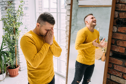 A man with bipolar disorder at the mirror. Bipolar affective disorder. A person with manic-depressive psychosis. Mental illness. A person with depression. A man is reflected in the mirror