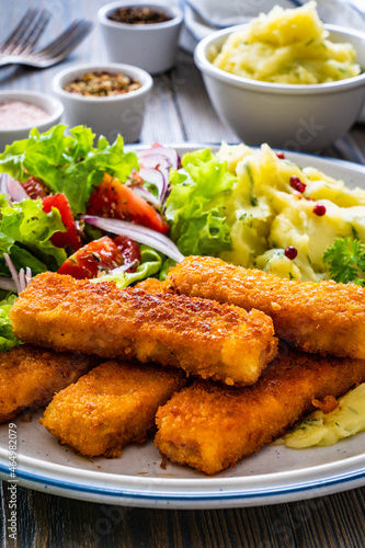 Fried fish sticks with potato puree and fresh vegetable salad on wooden table 