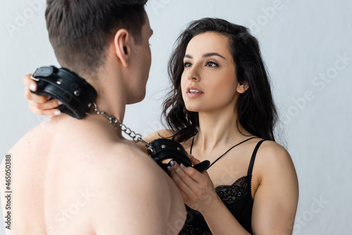 sexy and dominant woman holding leather handcuffs near shirtless man