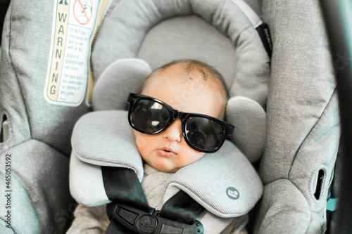 newborn baby boy wearing sunglasses in a gray carseat