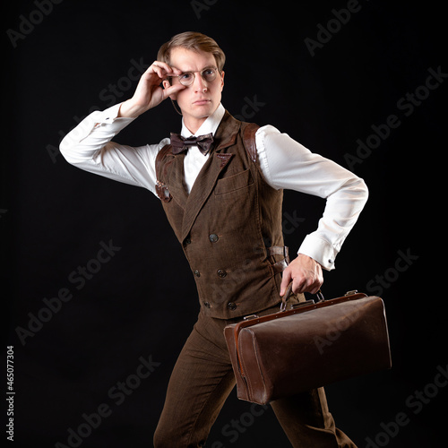 An intelligent gentleman in the Victorian style. Vintage retro suit, young attractive man in a vest and bow tie with glasses on a chain. he holds his bag in his hands, in a hurry, running somewhere