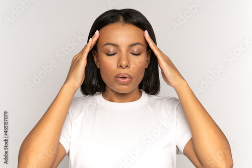Stressed young woman massaging temples and breathing in deeply to relief from emotional stress, anxiety or disorder. Anxious female with closed eyes touching head suffer from hard headache or migraine