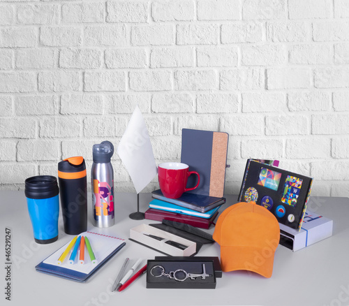 Composition of different promo products - Thermo mug, mug, gifts, pens in boxes, notebooks, tools, cap,flag table. Copy space. Grey wall background.