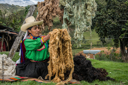 Mujer latinoamericana andina colgando lana de oveja teñida de colores en el campo para secarla en Cañaris Perú
