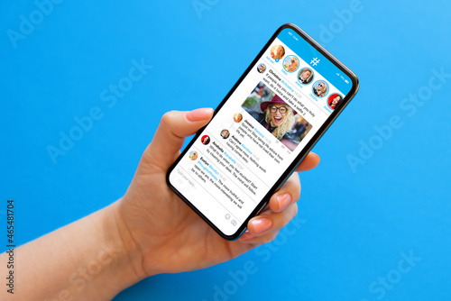 Person holding mobile phone in hand on blue background with sample social media microblogging app on the screen