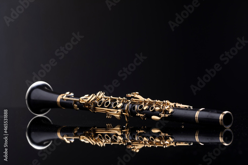 A full size clarinet with gold plated keys laying on a reflective surface with a dark background. A woodwind instrument common to classical music.