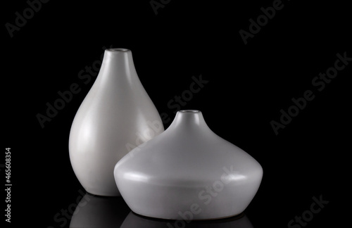 Two curvy white vases on black, with reflection.