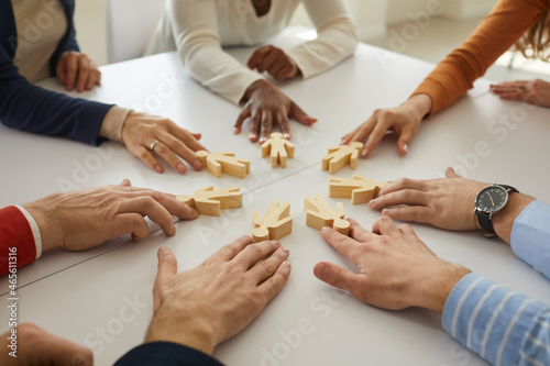 Group of multiethnic business people and teammates sitting around office table put little wooden human figures in circle as symbol of community, team, help, cooperation, collaboration and teamwork