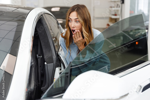 Happy astonished woman customer female buyer client wears blue shirt open door chooses auto wants to buy new automobile in car showroom vehicle salon dealership store motor show indoor. Sales concept.