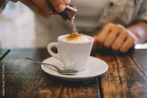 Close up hands putting white sugar in an italian espresso coffee at the bar or restaurant ona wooden table. Italian tradition and arabic. Cafe' leisure activity and breakfast morning