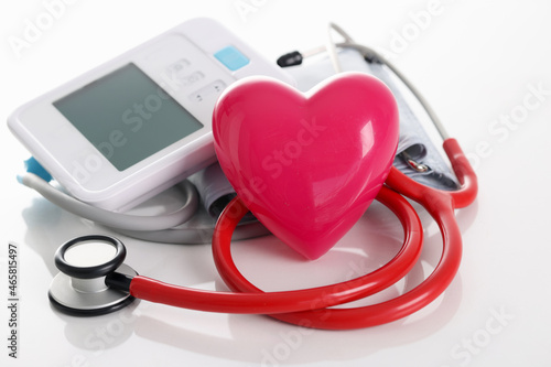 Toy red heart lying near electronic tonometer and stethoscope closeup