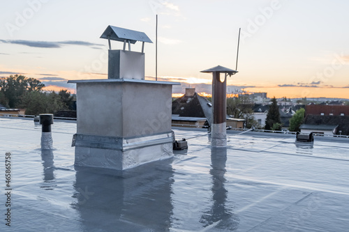 Flat roof covered with bitumen membrane and silver lacquer with chimney on a private house. Reflections after rain