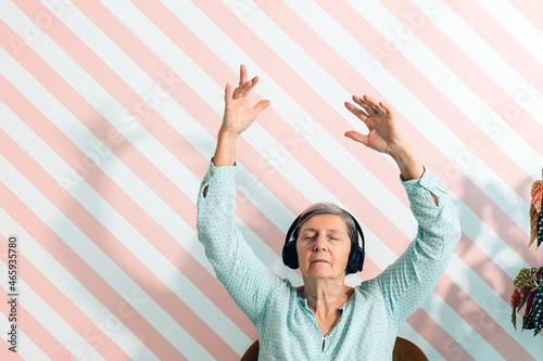 elderly lady in her seventies listens to music with headphones moving her arms in the air and letting herself be carried away by the sound keeping her eyes closed - leisure time