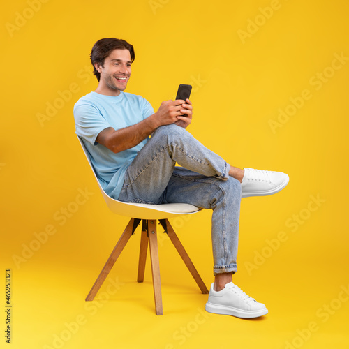 Happy guy using mobile phone at studio, sitting on chair