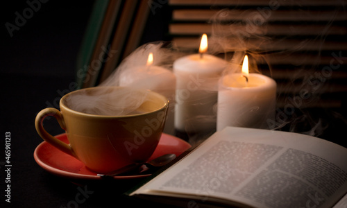cup of coffee with smoke and candles alfon with books (focus on cup)