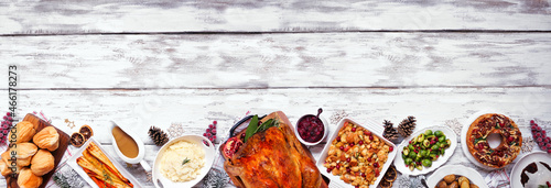 Classic Christmas turkey dinner. Above view bottom border on a white wood banner background. Turkey, potatoes and sides, dressing, fruit cake and plum pudding.