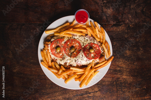 Overhead view of a Neapolitan-style milanesa with french fries on a plate on a wooden table.