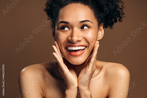 Natural beauty. Portrait of overjoyed multiracial brunette girl with perfect skin and nude makeup posing over brown studio background while looking away