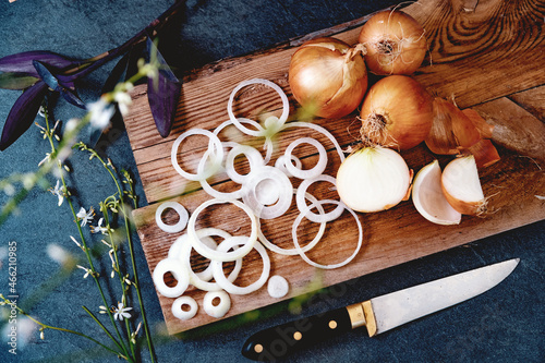 Cebollas y rodajas doradas sobre tabla de cortar de madera.Fondo de comida sana. Un montón de cebollas en una cesta y platos en un fondo de textura oscura y elegante.