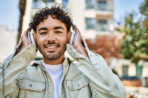 Handsome hispanic man with beard smiling happy outdoors on a sunny day wearing headphones