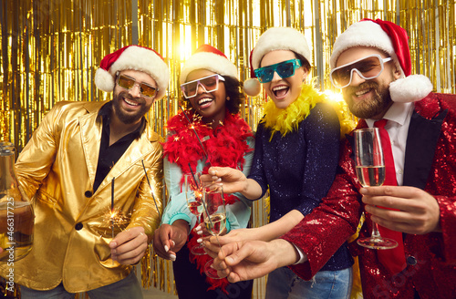New year eve winter holiday celebration. Happy smiling friends merry christmas disco people group in party santa claus hat holding sparklers, xmas wine glasses posing for camera on glitter background