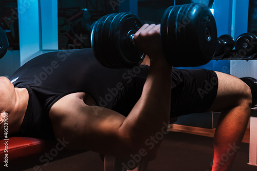 A young athlete lies on a bench and lifts heavy dumbbells. 
