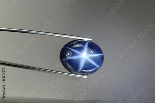 Natural 6 rays blue star sapphire gemstone in tweezers. Heated, diffusion treated, opaque, oval cabochon polished loose setting for making jewelry. Natural mined genuine corundum. Gemology, mineralogy