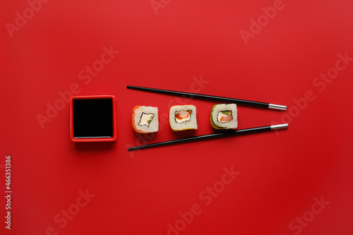 Delicious sushi rolls, chopsticks and bowl with soy sauce on color background