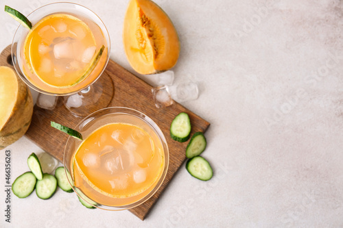 Glasses of cold cocktail, slices of cucumber and melon on light background