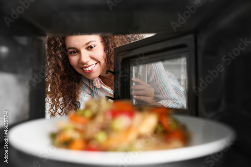 Young African-American woman heating food in microwave oven, view from inside