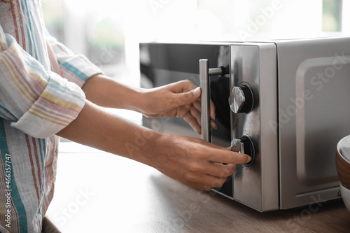 Young woman adjusting microwave oven in kitchen, closeup