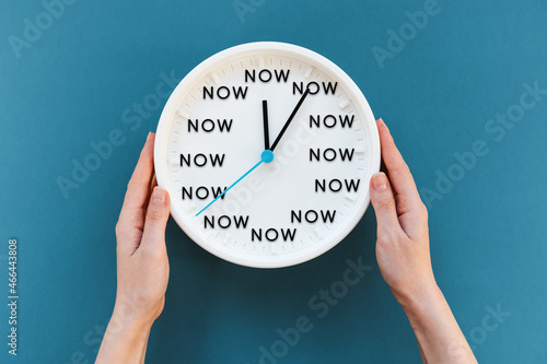 Woman's hands hold a watch with the inscription NOW. Blue background. Flat lay. The concept of time management and procrastination