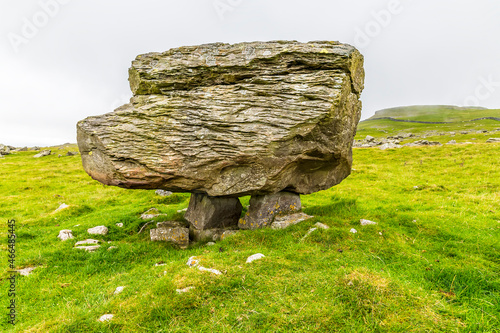 A side view showing a glacial erratic supported on the limestone pavement on the southern slopes of Ingleborough, Yorkshire, UK in summertime