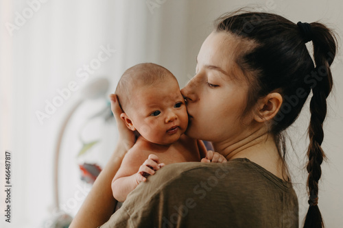 Loving mother carying of her newborn baby at home. Bright portrait of happy mum holding cute infant child on hands. Mother hugging her little 1 months old daughter.