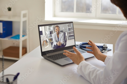Online doctor sitting at table with laptop computer and stethoscope and counseling young female patient via video call. Telemedicine, professional online consultation, medical teleconference concept