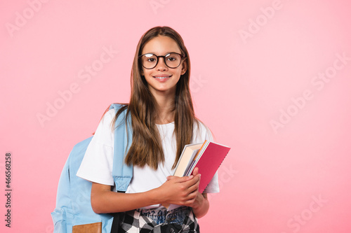 Smiling active excellent best student schoolgirl holding books and copybooks going to school wearing glasses and bag isolated in pink background