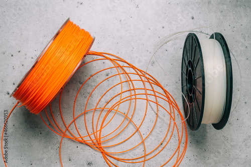 3D Printer Plastic Filaments. Spools of orange and white thermoplastic wires for 3D printing close up on grey stone background
