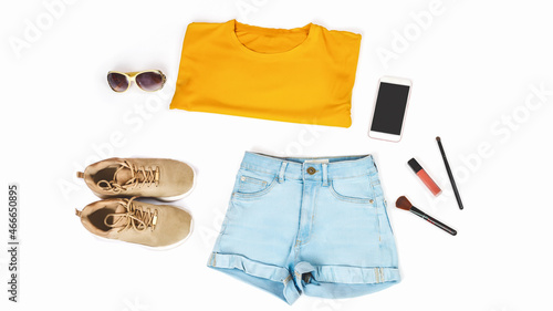 Women's summer clothes and accessories: orange t-shirt, denim shorts, sneakers, lipstick isolated on a light background, top view. Fashion beauty concept