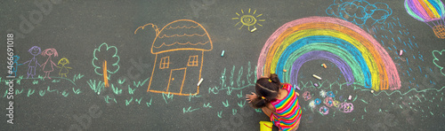 The child draws with chalk on the asphalt. Selective focus.