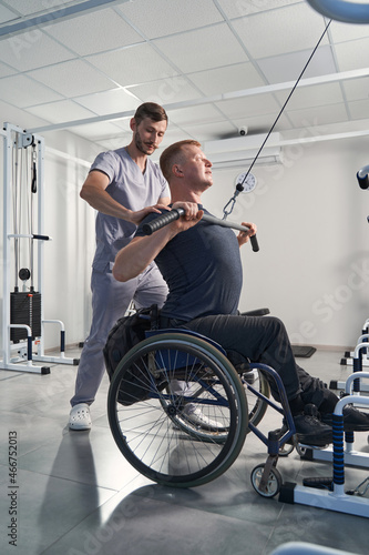 Physical therapist help wheelchair patient in gym. Man with paraplegia