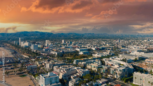 an aerial shot of the cityscape of the City of Santa Monica with vast miles of buildings and palm trees with majestic mountain ranges and powerful clouds at sunset in Santa Monica California USA
