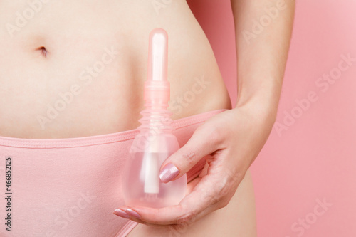 Concept of Gynecology, woman health. Vaginal enema in woman's hand on pink background near her body. Treatment of vaginal infections from candidiasis, thrush, sexually transmitted infections