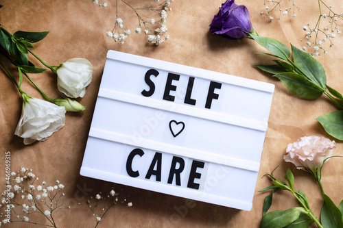 Self-care word on lightbox and flowers on color background flat lay. Take care of yourself