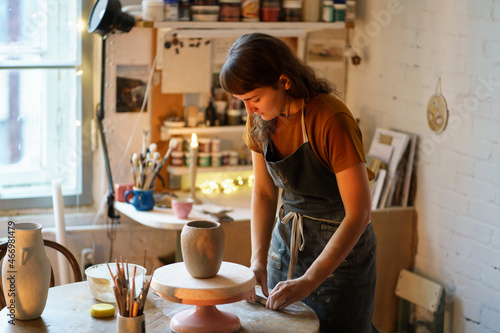 Art therapy for hobby or small business: young woman work in ceramics studio on handicraft jar production for handmade pottery shop. Artisan female shaping tableware from raw clay in workshop space