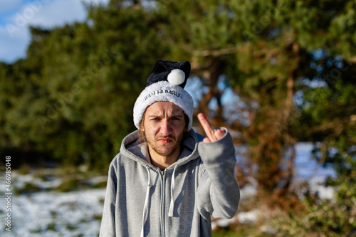 A grumpy young man wearing a black santa hat with the words Bah Humbug written on it